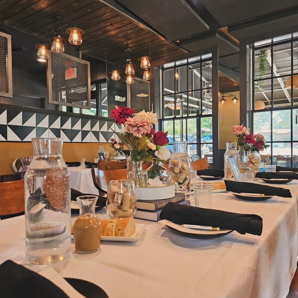 Elegantly set restaurant table with floral centerpieces, black place settings, and warm lighting in a stylish dining room.