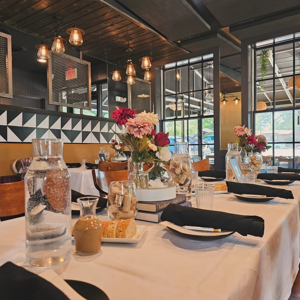 Elegantly set restaurant table with floral centerpieces, black place settings, and warm lighting in a stylish dining room.