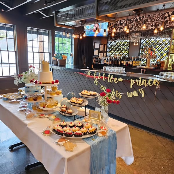 Dessert table with cake, cupcakes, and cookies for a "little prince" baby shower in a restaurant.