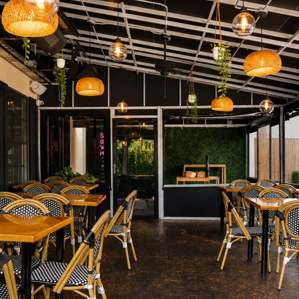 Spacious outdoor restaurant patio with wooden tables, woven chairs, and hanging wicker lights.