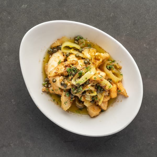 Fried calamari with capers, onions, and parsley in a white bowl on a dark surface.