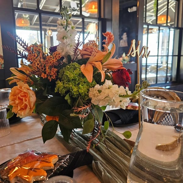 Vibrant floral centerpiece with orange, white, and green flowers on a restaurant dining table with a 'Six' sign.
