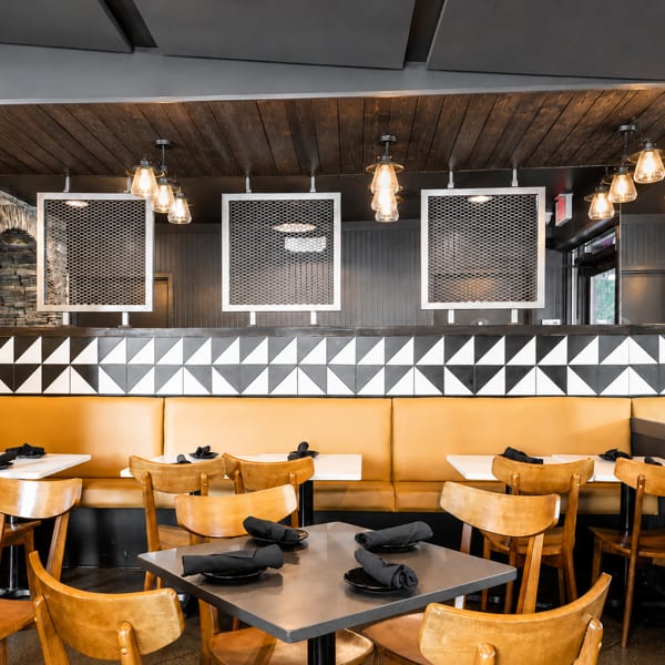Modern restaurant interior with yellow booths, wooden chairs, geometric wall tiles, and industrial lighting.