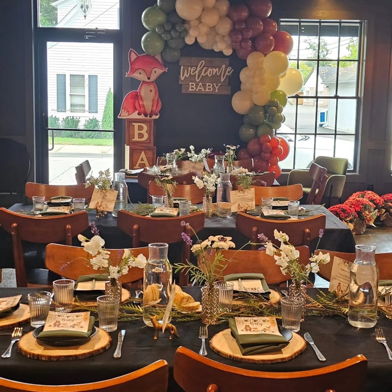 Tables set for a baby shower with fox decor, balloon arch, and floral centerpieces.
