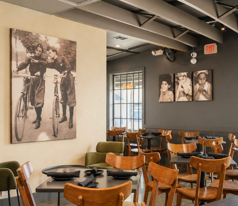Restaurant dining room with wooden chairs, dark tables, and vintage-style artwork on the walls.