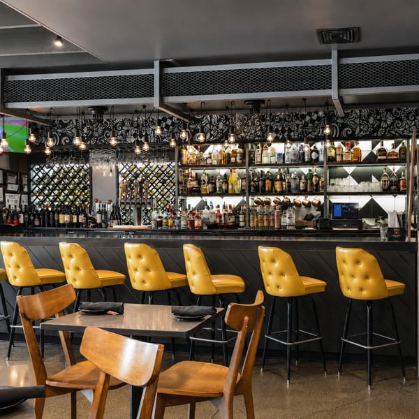 Stylish restaurant bar with bright yellow stools, a full liquor selection, and ambient lighting.