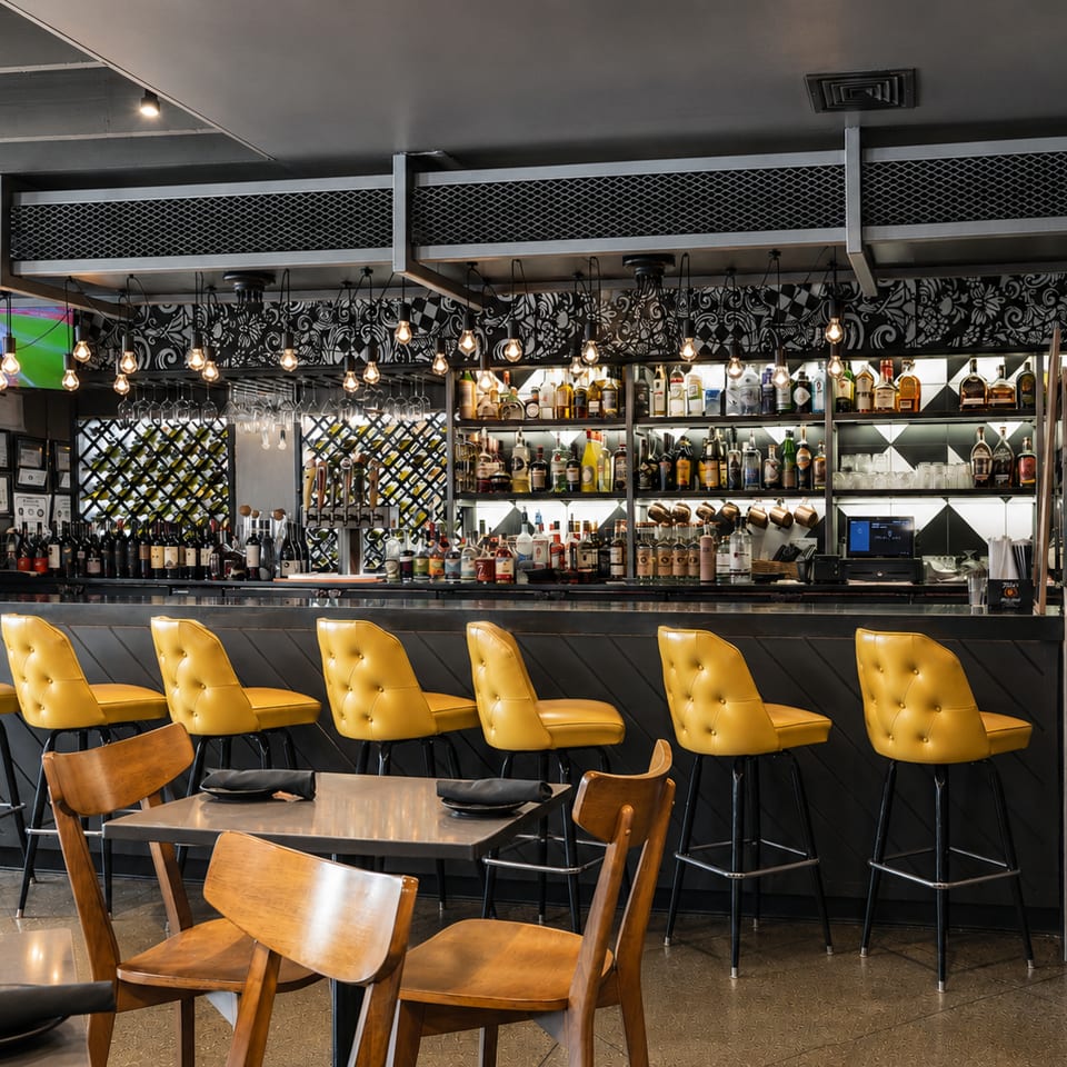 Stylish restaurant bar with bright yellow stools, a full liquor selection, and ambient lighting.