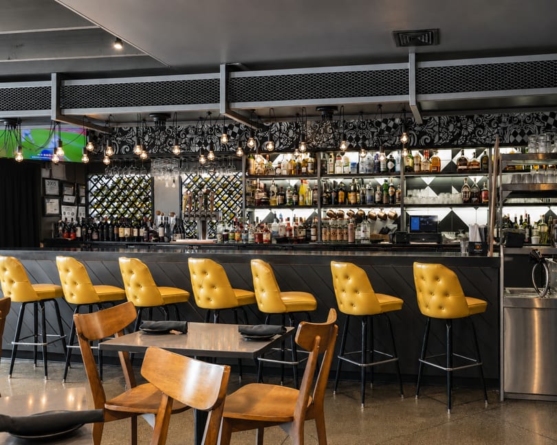 Stylish restaurant bar with bright yellow stools, a full liquor selection, and ambient lighting.