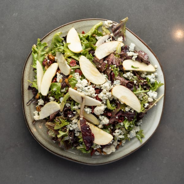 Overhead view of a fresh salad with mixed greens, pear slices, blue cheese, cranberries, and walnuts.