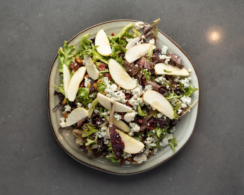 Overhead view of a fresh salad with mixed greens, pear slices, blue cheese, cranberries, and walnuts.