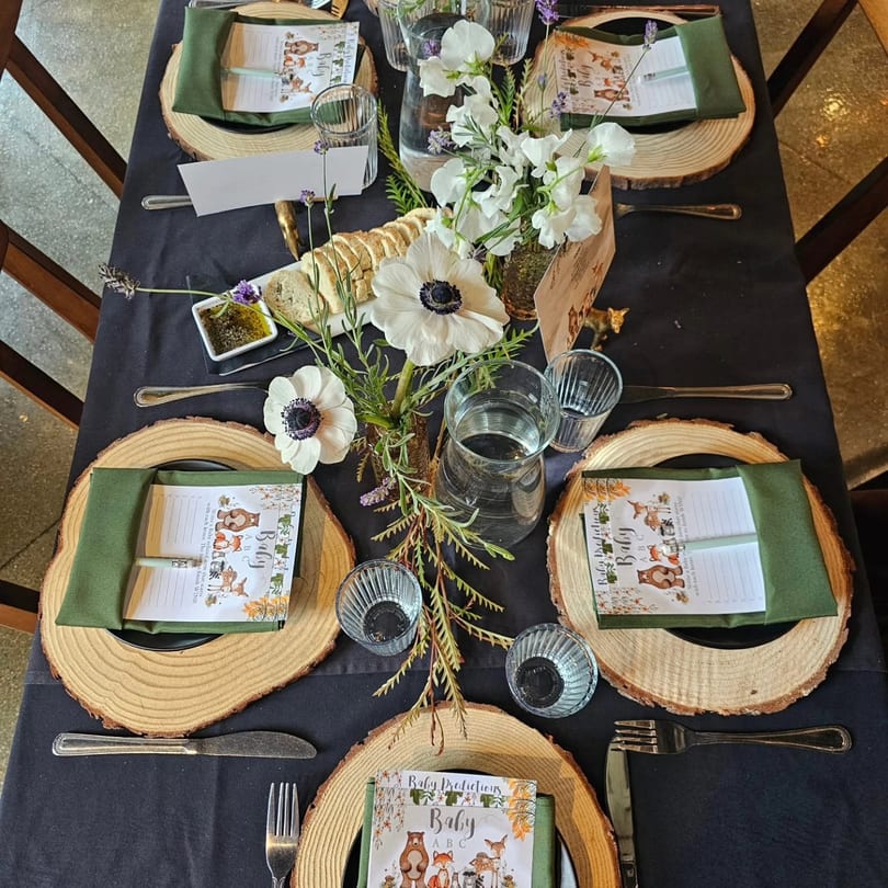 Woodland-themed baby shower table with wooden chargers, green napkins, white flowers, and bread.