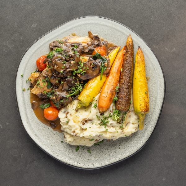 Chicken with mushroom gravy, mashed potatoes, roasted carrots, and cherry tomatoes on a plate.