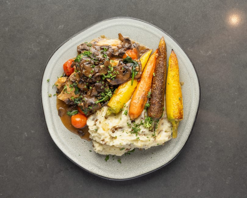 Chicken with mushroom gravy, mashed potatoes, roasted carrots, and cherry tomatoes on a plate.